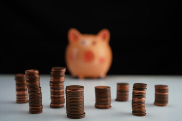 general view with detail of stacked coins of different currencies in front of an out-of-focus piggy bank in the background as a concept of saving for home purchase