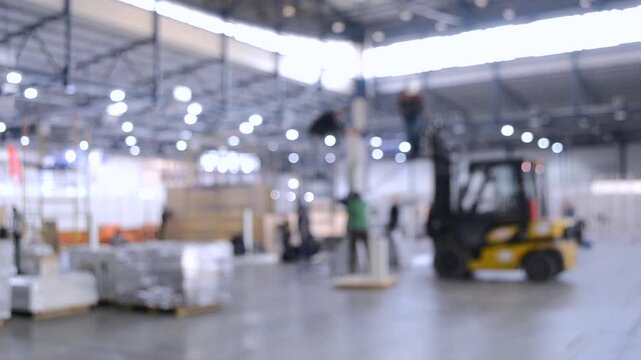 Construction works inside large building. Building installation exhibition center. Loader machine on the construction site. Many people in installation work. Blurred Background