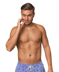 Naklejka premium Young man shirtless in swimwear, studio with fingers on lips keeping a secret.