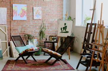 No people shot of modern art studio interior equipped with easels and comfortable wooden chairs, decorated with vintage carpet and paintings
