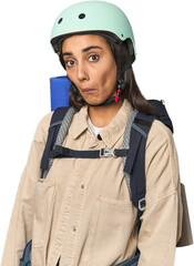 Hispanic young woman with mountain gear shrugs shoulders and open eyes confused.