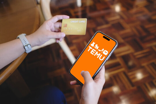 Bangkok. Thailand. Aug 7 2024 : A wowan useing credit card and open Temu app is seen on an iPhone 15. Temu is an online marketplace and a subsidiary of China-based e-commerce platform Pinduoduo.