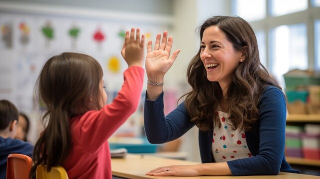 Happy teacher and schoolgirl giving high five during class at school.