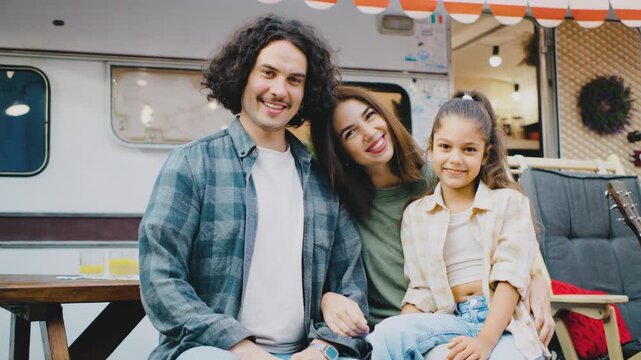 Capture a joyful family portrait in front of a vintage camper, surrounded by nature, showcasing their happiness and bond during a summer outing filled with laughter and lasting memories