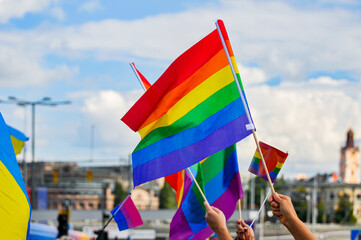 Cropped image of people holding rainbow flag against sky