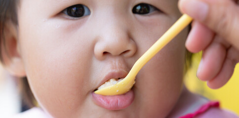 Mother feeding child,Baby girl eating blend mashed food sitting, on high chair, mother feeding child, hand with spoon for vegetable lunch, baby weaning, first solid food for