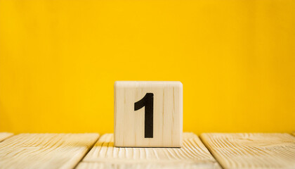 Wooden cube with number 1 one on wooden table with yellow wall on background. Close-up.