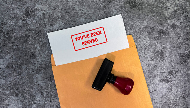 Red Handle Rubber Stamper and You've been served text above brown envelope isolated on wooden background