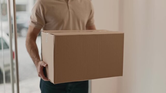 A faceless delivery man in casual attire holding a large cardboard package, delivering a shipment to apartment adress
