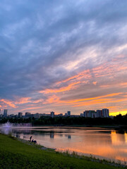 Fototapeta premium A stunning sunset gracefully casts its colors over a serene lake, while a vibrant city skyline stands majestically in the background, creating a picturesque blend of nature and urban life