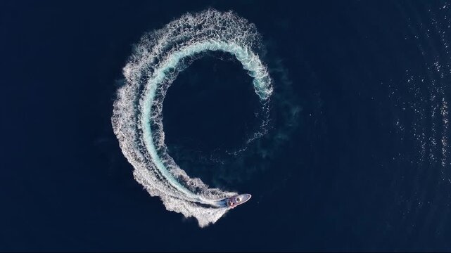 Aerial top view of a motor RIB boat forming a circle of waves and bubbles with its engine over the blue sea