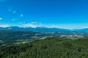 Fototapeta premium Panoramic view of majestic mountain range Karawanks in summer seen from tower Pyramidenkogel, Carinthia, Austria. Fog covered alpine valley surrounded by majestic Austrian Alps. Mystical atmosphere