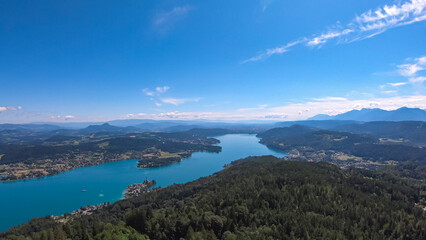 Obraz premium Aerial panoramic view of Lake Wörthersee seen from Pyramindenkogel in Carinthia, Austria. Serene turquoise waters, lush green forests and rolling hills of Austrian Alps. Charming lakeside village