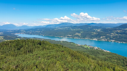 Aerial panoramic view of Lake Wörthersee seen from Pyramindenkogel in Carinthia, Austria. Serene turquoise waters, lush green forests and rolling hills of Austrian Alps. Charming lakeside village
