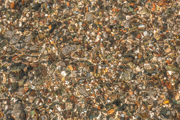 multi-colored stones under water on the sea, river. Natural background of stones, glare on the water
