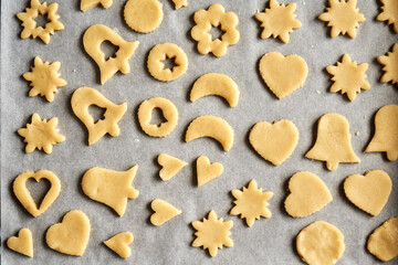 Shapes cut out of raw pastry dough on a sheet of baking paper - preparation of traditional Linzer Christmas cookies