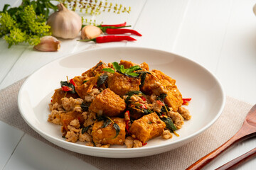 Stir fried basil with minced pork and Deep Fried Hard tofu soy bean curd in white plate.