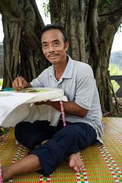 Elderly Vietnamese man sewing under a large tree