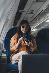Fototapeta premium A young Asian woman, seated as an airplane passenger, contemplates dollar bills, reflecting on lucrative opportunities and aspirations towards billionaire status.