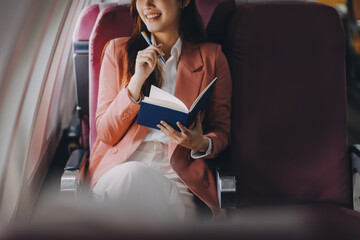 Attractive Asian female passenger of airplane sitting in comfortable seat while working laptop and...