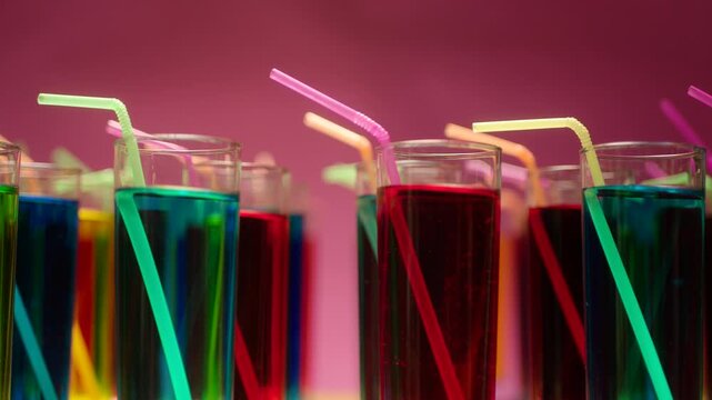 Row of many glasses with colorful drinks vibrating on pink background . Different alcohol cocktails or fresh fruit juices inside crystal cups with moving or shaking straws . Birthday party celebration