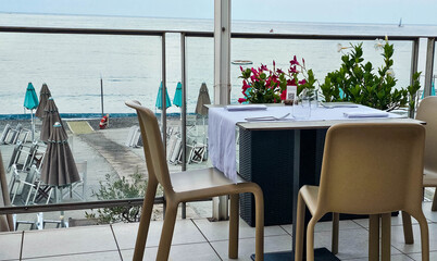 tables set for an elegant dinner in a restaurant with sea view on the beach of the Ligurian Riviera in the summer of 2024