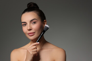 Fototapeta premium Beautiful woman with makeup brush on grey background. Space for text