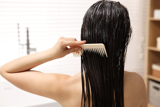 Woman combing her hair with applied mask in bathroom, back view