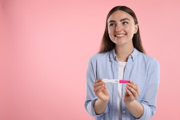 Happy woman holding pregnancy test on pink background, space for text