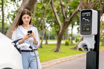 Young woman using smartphone online banking application to pay for electric car battery charging...