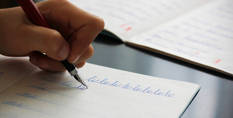 Detail of a child's left hand writing the syllables li and le with a fountain pen in a copybook....