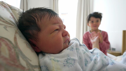 Close-up newborn baby during first week of life with brother playing in background, family lifestyle scene