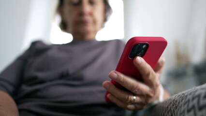 Close-up of senior woman's hand holding cellphone device seated at home couch, person reading content online, technology phone