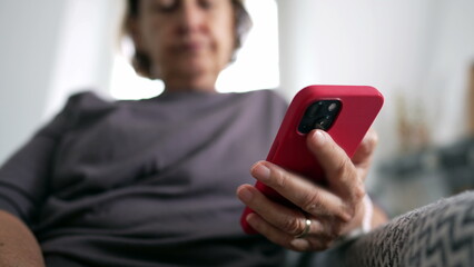 Close-up of senior woman's hand holding cellphone device seated at home couch, person reading content online, technology phone