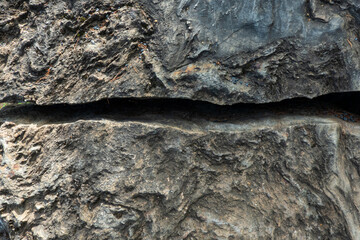 A wide horizontal crack divides the dark grey surface of the rough stone in half. Background....