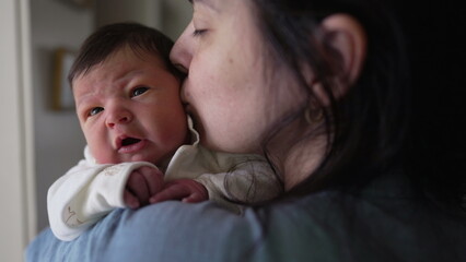 Mother holding newborn baby in arms during first week of life, nurturing maternal caring love of...