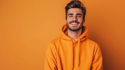 Obraz premium smiling man in orange hoodie looking at camera isolated on orange