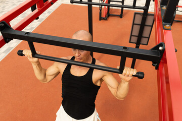 Athlete muscular fitness male pulling up on horizontal bar at street gym. Outdoors. Summer. Workout routine.
