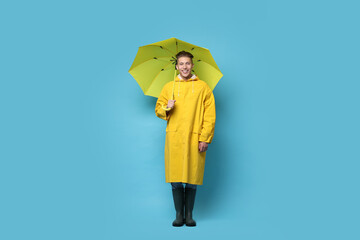 Young man with yellow umbrella on light blue background