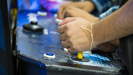 Detail on Hands with Arcade Joystick Playing Old Arcade Video Game. Detail of player hand interacting and playing with joysticks and buttons on an old arcade game in a gaming room © Octavio