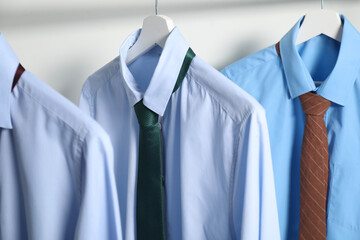 Hangers with shirts and neckties on light background, closeup