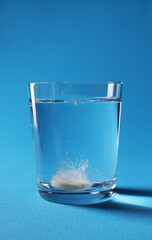 Effervescent pill dissolving in glass of water on light blue background