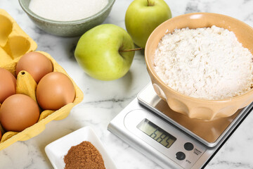 Kitchen scale with bowl of flour and products on white marble table, closeup