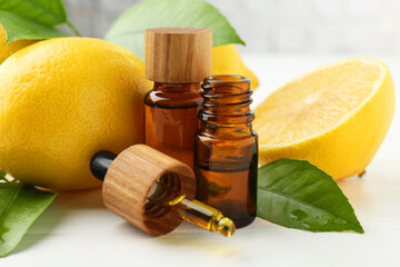 Essential oils in bottles, dropper, lemons and green leaves on white table, closeup