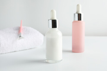 Bottles of chemical peel, towel and brush on light background, closeup. Peeling procedure