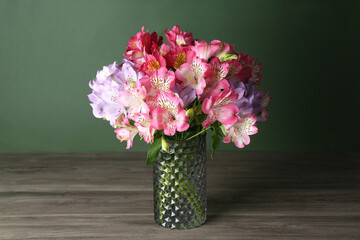 Beautiful alstroemeria flowers in vase on wooden table against green background