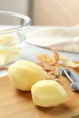 Fresh raw potatoes, peels and peeler on table