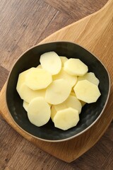 Cut fresh raw potatoes in bowl on wooden table, top view