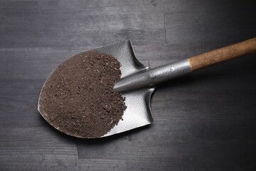 Metal shovel with soil on black wooden table, top view