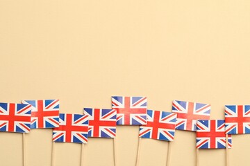 Small paper flags of United Kingdom on beige background, top view. Space for text